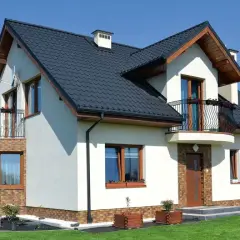 Nowoczesny dom z balkonem i wykuszą, który dodaje mu uroku. Elegancka bryła, ciemny dach i jasne ściany.