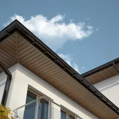 Elegancka podbitka dachu z brązowymi rynnami, widok z dołu na tle błękitnego nieba z chmurami.