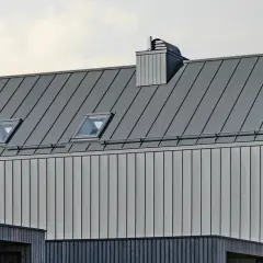 Nowoczesny dach z blachy na rąbek, z oknami dachowymi i kominem. Sprawdź blacha na rąbek cena m2.
