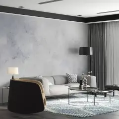 Nowoczesny salon z szarą kanapą i fotelami. Ściana ozdobiona tapetą imitującą beton, wykonaną z flizeliny.