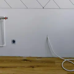 Białe rury wodne i zawór na ścianie, gniazdka elektryczne i biały kabel zwinięty na drewnianej podłodze. Instalacja gazowa w domu w trakcie prac.