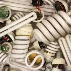 Stos zużytych żarówek energooszczędnych, w tym spiralnych i prostych jarzeniówek, z widocznymi elementami elektronicznymi.