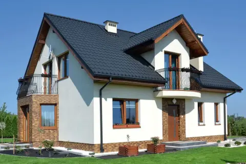 Nowoczesny dom z balkonem i wykuszą, który dodaje mu uroku. Elegancka bryła, ciemny dach i jasne ściany.