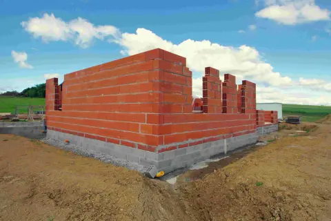 Budowa domu w toku: czerwone ściany z pustaków i betonowy fundament. Zastanawiasz się, ile trwa budowa domu?