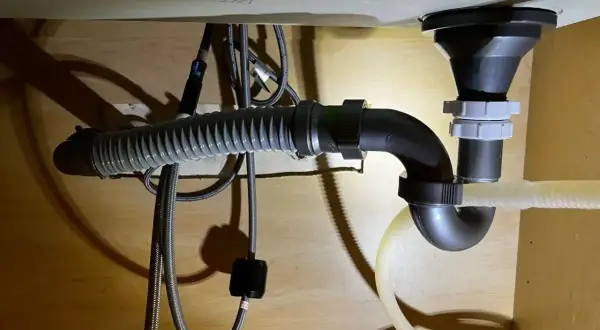 Pod zlewem widać instalację hydrauliczną z syfonem i elastycznym wężem odpływowym. Widać też trójnik, który rozdziela odpływ.