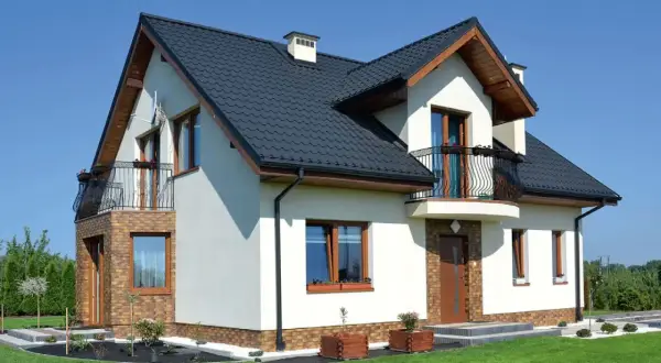 Nowoczesny dom z balkonem i wykuszą, który dodaje mu uroku. Elegancka bryła, ciemny dach i jasne ściany.