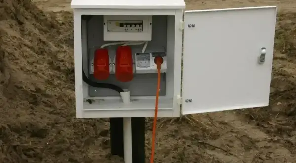 Skrzynka elektryczna na działce bez domu, gotowa do podłączenia prądu. W środku bezpieczniki i gniazda.