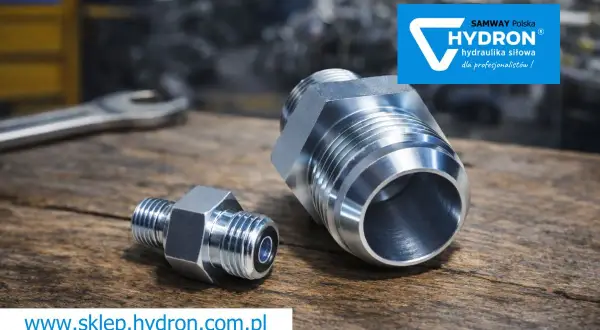 Metalowe złączki hydrauliczne, w tym nypel, leżą na drewnianym blacie. Obok klucz. Logo Hydron.
