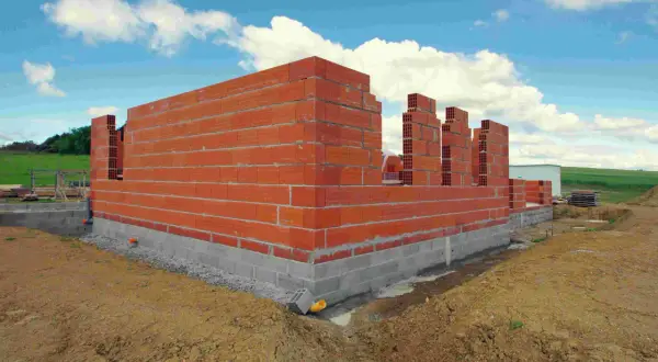 Budowa domu w toku: czerwone ściany z pustaków i betonowy fundament. Zastanawiasz się, ile trwa budowa domu?