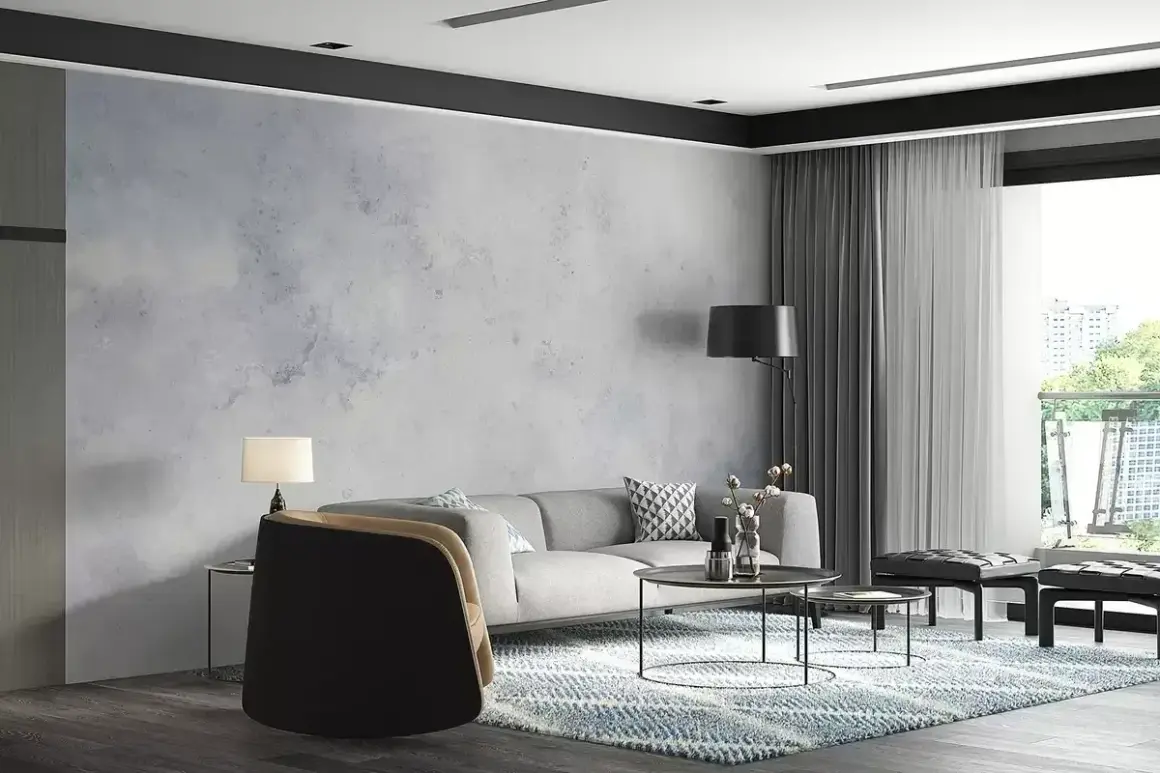 Nowoczesny salon z szarą kanapą i fotelami. Ściana ozdobiona tapetą imitującą beton, wykonaną z flizeliny.