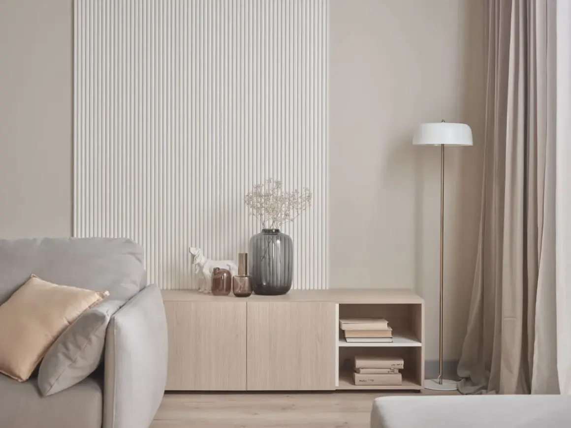 Nowoczesna ściana z ryflowaniem, komoda z książkami i wazonem, obok sofa. Idealne co na ścianę do salonu.