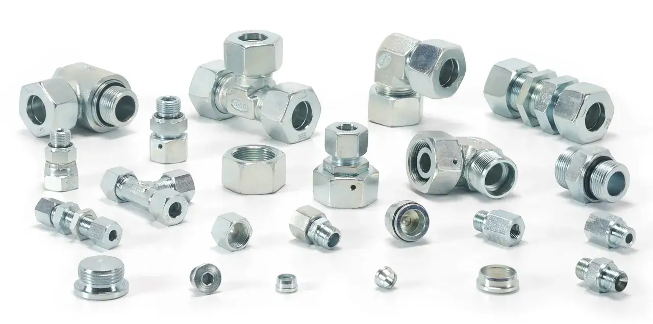 Metalowe złączki hydrauliczne, w tym kolanka, trójniki i redukcje. Wśród nich widać nypel do połączeń.