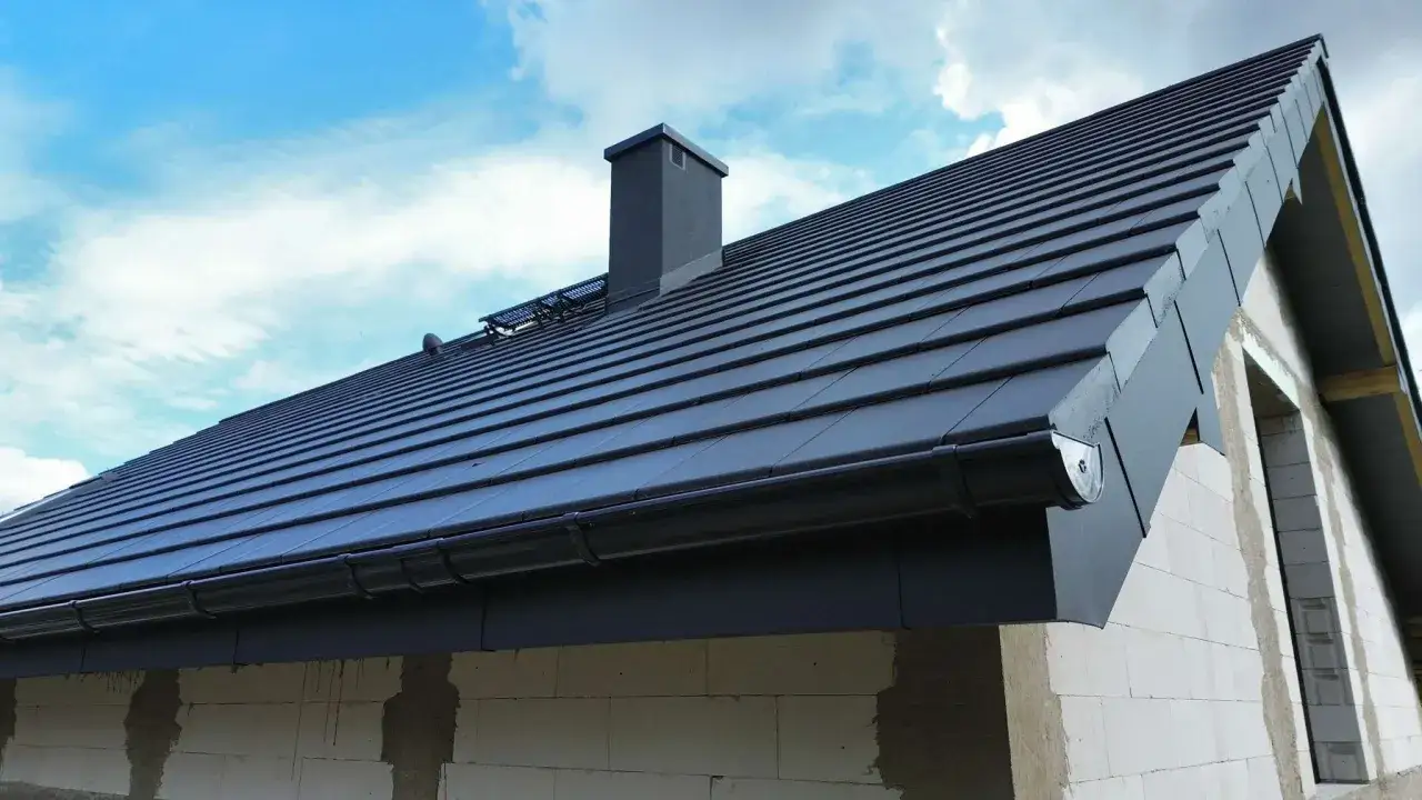 Nowoczesny dach z ciemnoszarych dachówek ceramicznych, z kominem i rynnami. Różne rodzaje dachówek ceramicznych dostępne są w wielu kolorach.