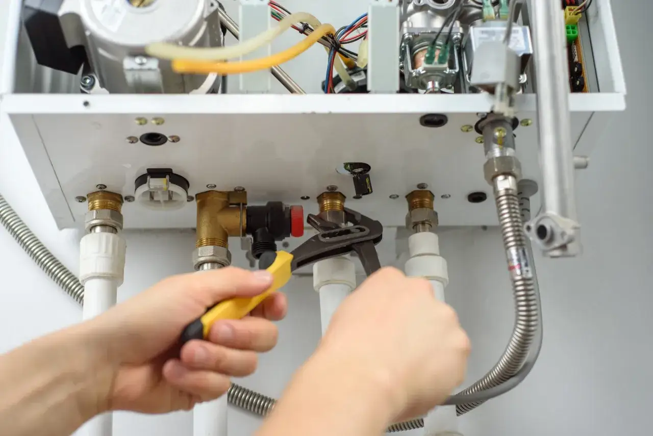 Ręce majsterkowicza dokręcają kluczem elementy instalacji gazowej w domu.