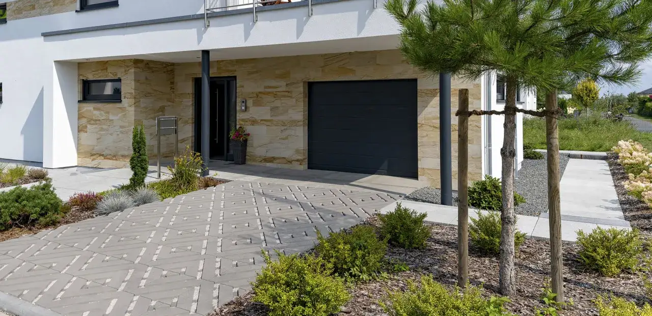 Nowoczesny podjazd do domu z betonowej kostki z geometrycznym wzorem, prowadzący do drzwi i garażu.