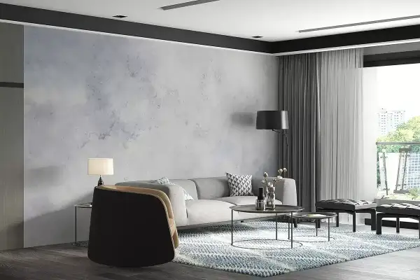 Nowoczesny salon z szarą kanapą i fotelami. Ściana ozdobiona tapetą imitującą beton, wykonaną z flizeliny.