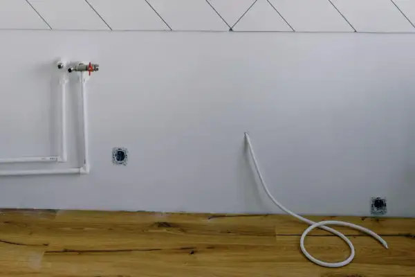 Białe rury wodne i zawór na ścianie, gniazdka elektryczne i biały kabel zwinięty na drewnianej podłodze. Instalacja gazowa w domu w trakcie prac.