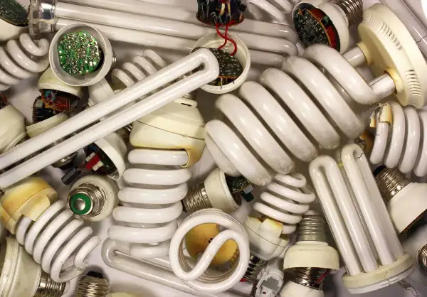 Stos zużytych żarówek energooszczędnych, w tym spiralnych i prostych jarzeniówek, z widocznymi elementami elektronicznymi.